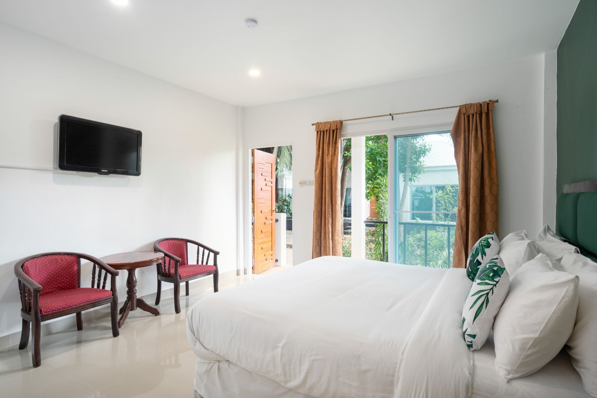 A hotel room with a bed, a TV mounted on the wall, a desk with a chair, and a view of the outdoors through a window.