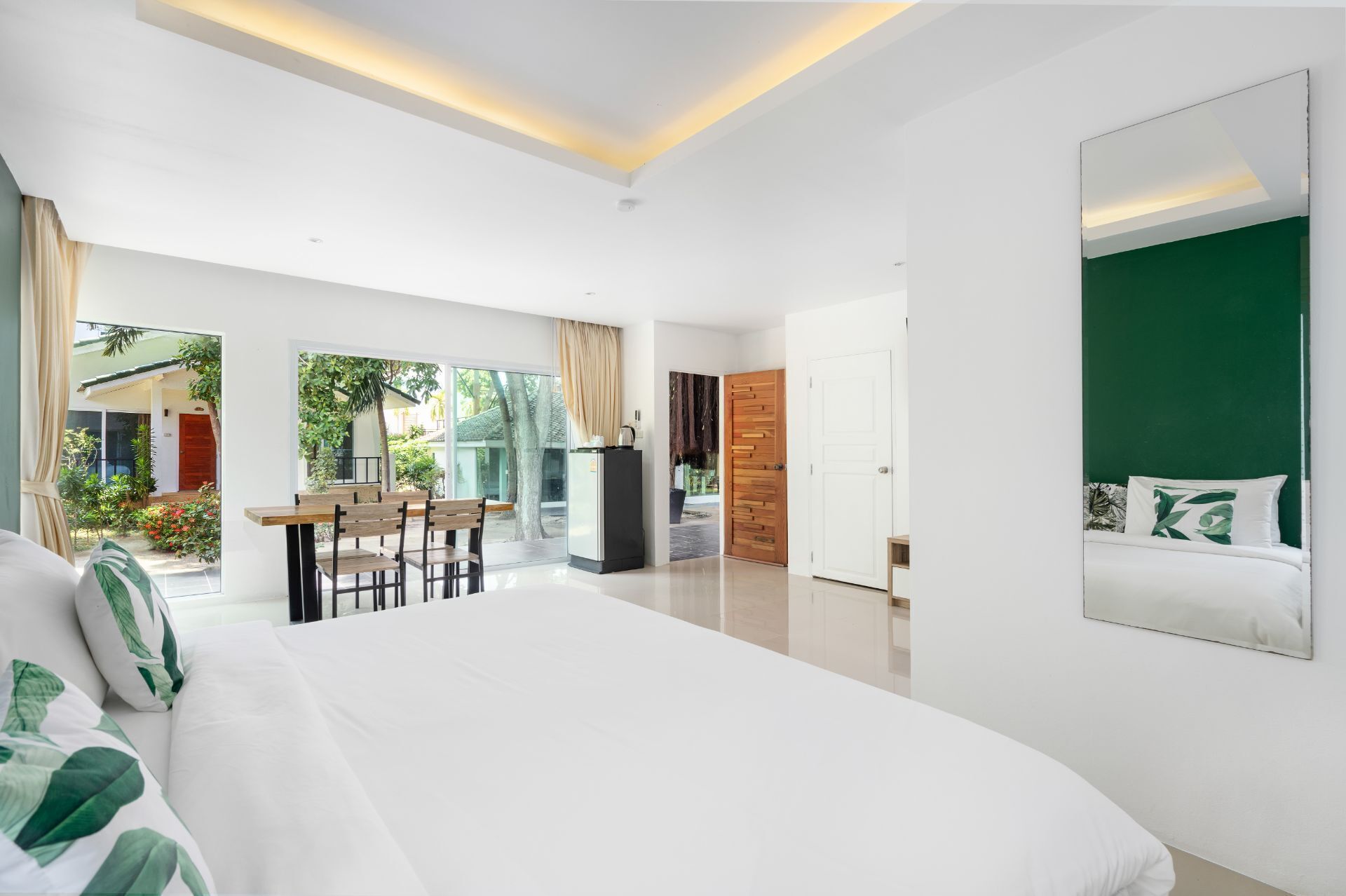 Quarto de hotel moderno com uma cama grande, área de refeições com mesa e cadeiras, e vista para o exterior.