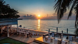 A poolside area with lounge chairs and umbrellas, overlooking a beach and the ocean. - 4U Resort Samui (Koh Samui)