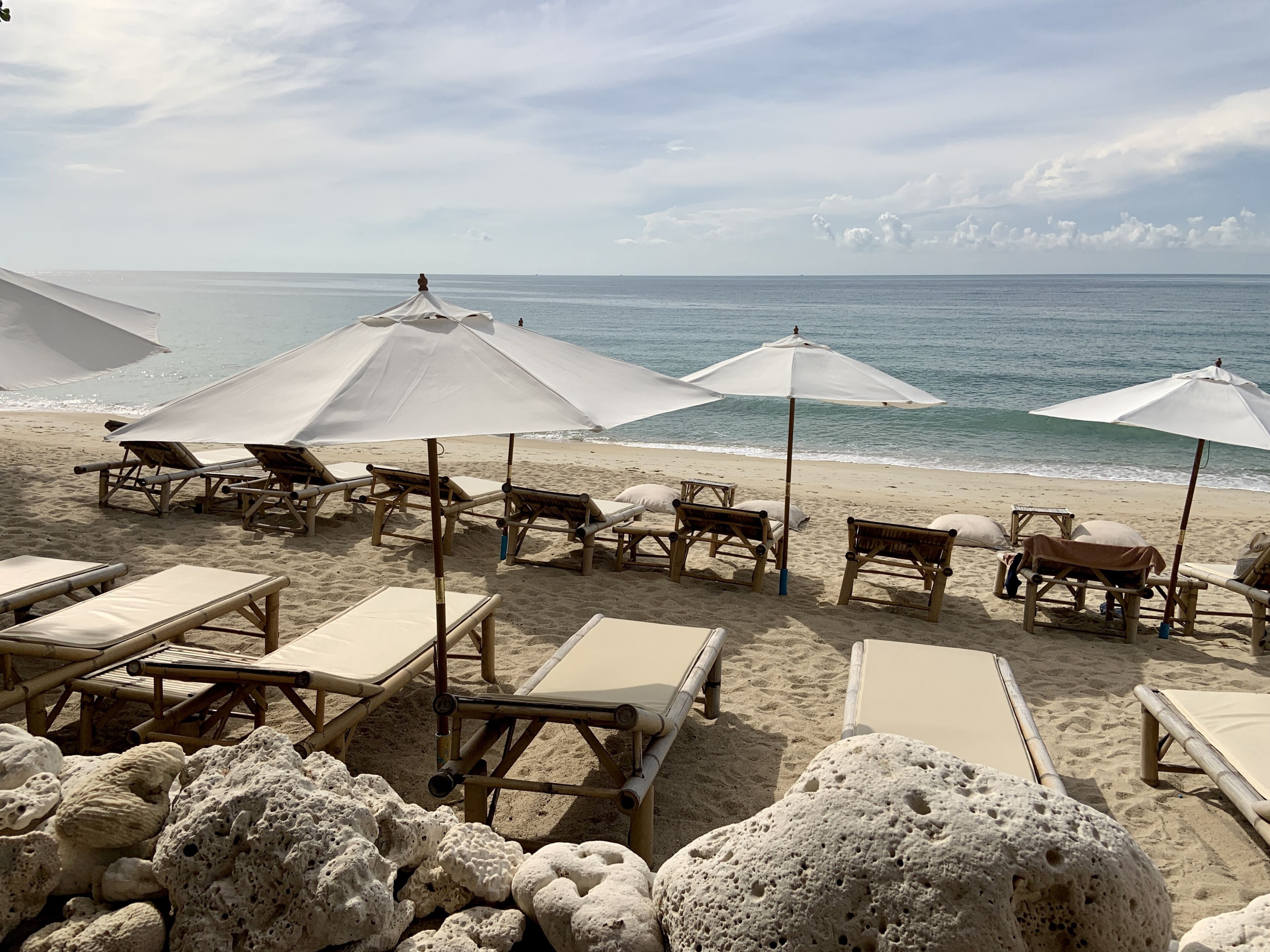 A beach with sun loungers and umbrellas, a sandy shore, and the ocean in the background.