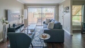 Un salon avec un canapé gris, une table basse, un téléviseur et un ventilateur de plafond.