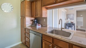Une cuisine avec des meubles en bois, un évier en acier inoxydable, un lave-vaisselle et une horloge au mur.