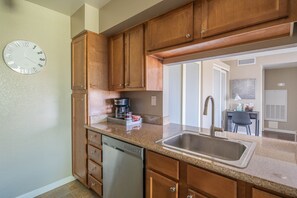 Kitchen area with a sink, dishwasher, and coffee maker, leading to a dining space with a table and chair.