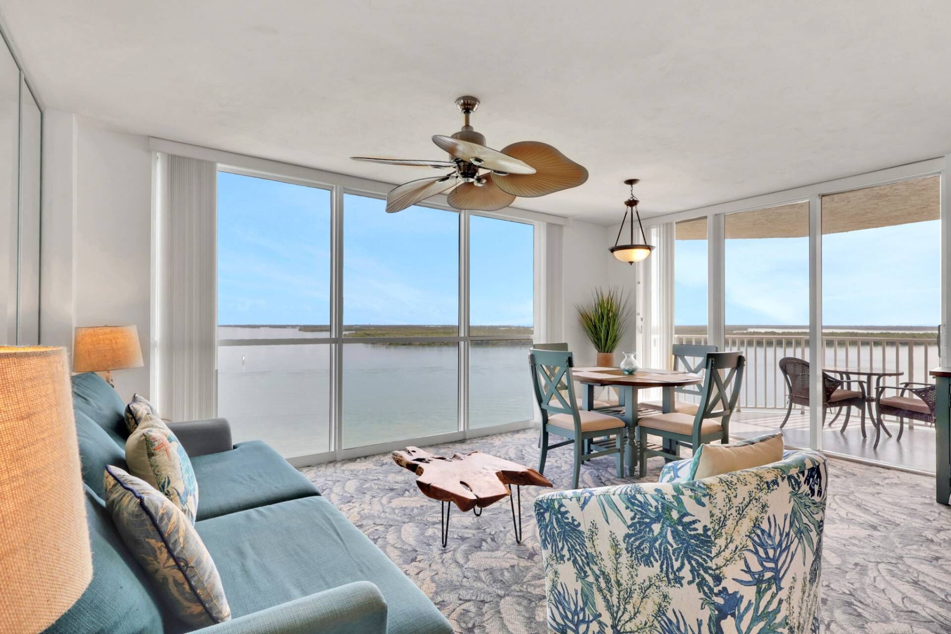 Un balcon spacieux avec vue sur l’eau, un ventilateur de plafond et un coin repas avec des chaises et une table.
