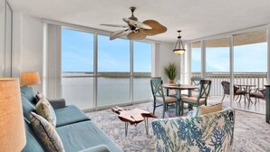 A spacious balcony with a view of the water, a ceiling fan, and a dining area with chairs and a table.