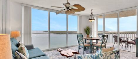 Un balcon spacieux avec vue sur l’eau, un ventilateur de plafond et un coin repas avec des chaises et une table.