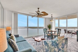 A spacious balcony with a view of the water, a ceiling fan, and a dining area with chairs and a table.