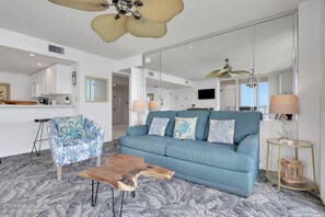 A living room with a blue sofa, a patterned armchair, a wooden coffee table, and a ceiling fan.