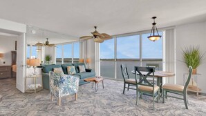 A spacious living room with a large window, a ceiling fan, and a dining area with chairs and a table.