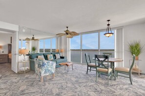 A spacious living room with a large window, a ceiling fan, and a dining area with chairs and a table.