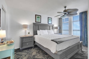 Une chambre d’hôtel avec un lit, des tables de chevet, un ventilateur de plafond et une fenêtre avec des stores.