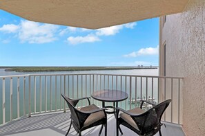 A balcony with a table and chairs, overlooking a calm body of water and distant buildings.