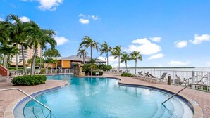 A swimming pool with a 3ft 3in depth, surrounded by palm trees and lounge chairs, with a view of the water and a building in the background.