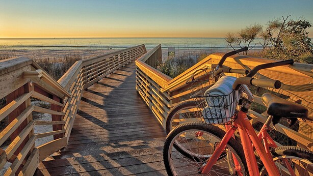 Una pasarela de madera que conduce a una playa, con una bicicleta estacionada a la derecha.