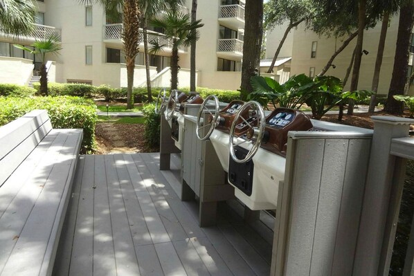A deck area with a row of stationary boats, a bench, and a pathway leading to a building with balconies.