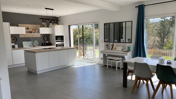 A modern kitchen with a central island, a dining area with a table and chairs, and a large sliding glass door leading to a patio.
