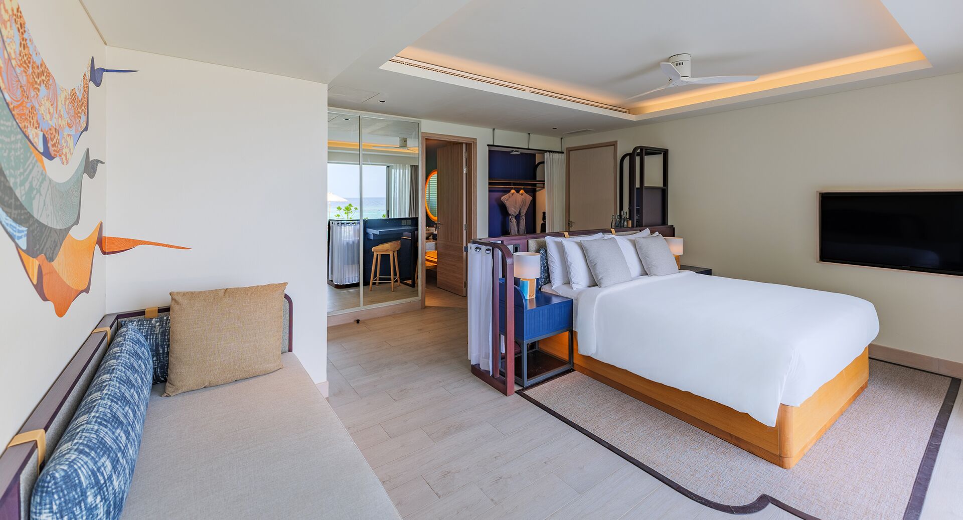 A modern hotel room with a large bed, a TV, and a view of the sea.
