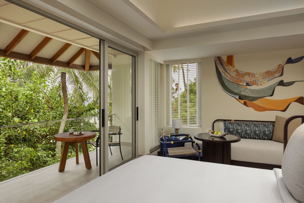 A modern hotel room with a balcony, a sofa, a small table, and a bed.
