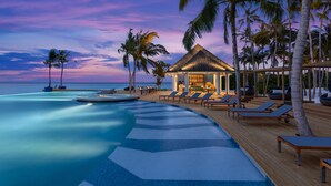 A resort pool area with lounge chairs and a small hut, surrounded by palm trees and overlooking the sea. - Avani+ Fares Maldives Resort (Fares)