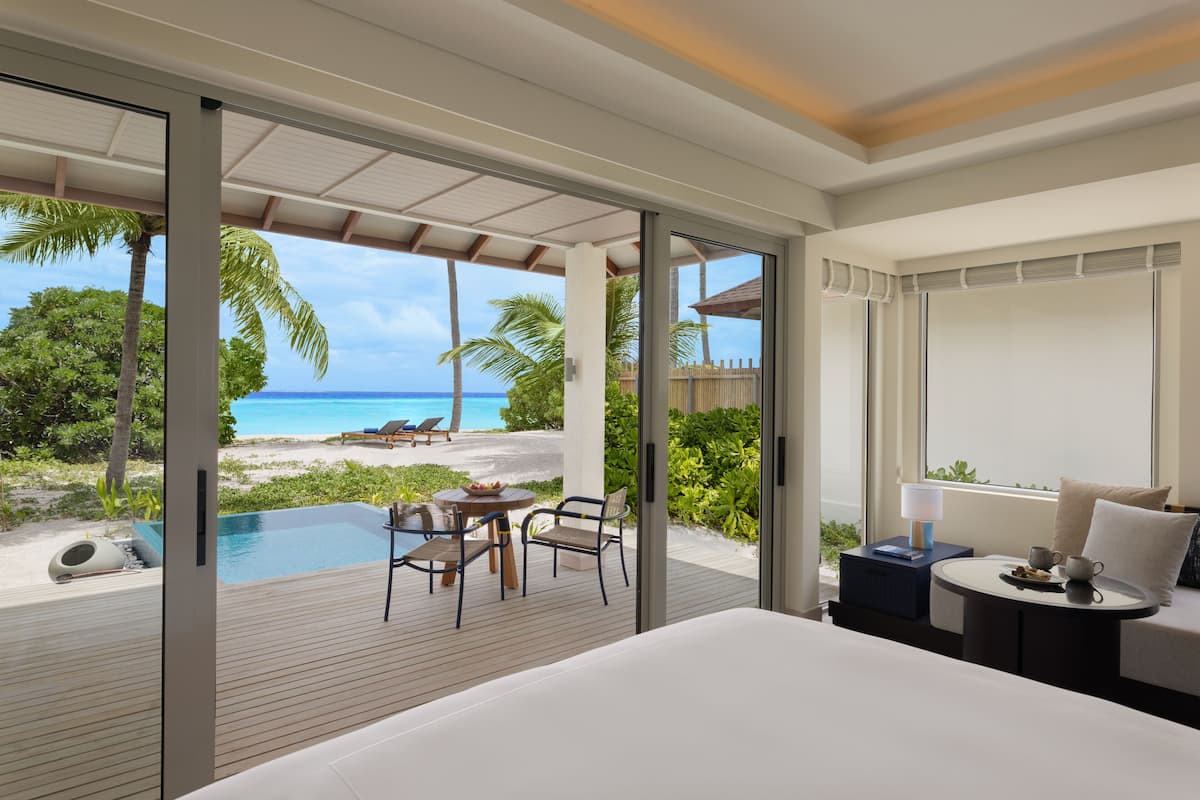 A bedroom with a view of the ocean, a pool, and a dining area with outdoor furniture.