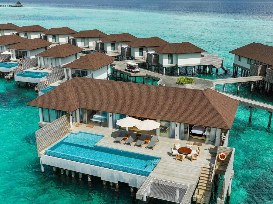 Overwater bungalows with infinity pools, connected by walkways, in a clear turquoise sea.