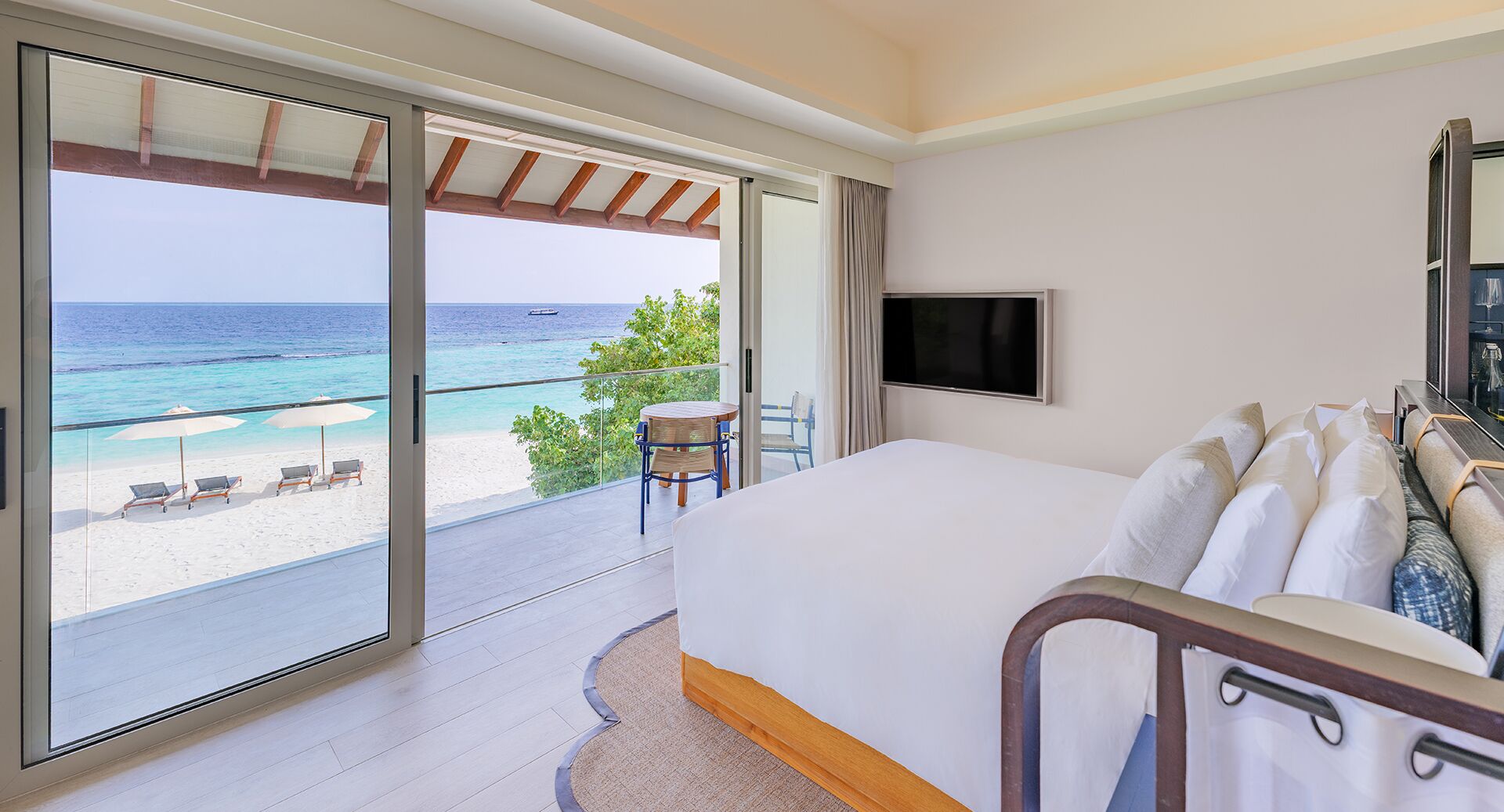 A hotel room with a large bed, a TV, and a balcony with a view of the beach and ocean.