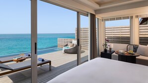 A modern hotel room with a large bed, a seating area with a table and chairs, a small side table with a lamp, and a view of the ocean. - Avani+ Fares Maldives Resort (Fares)