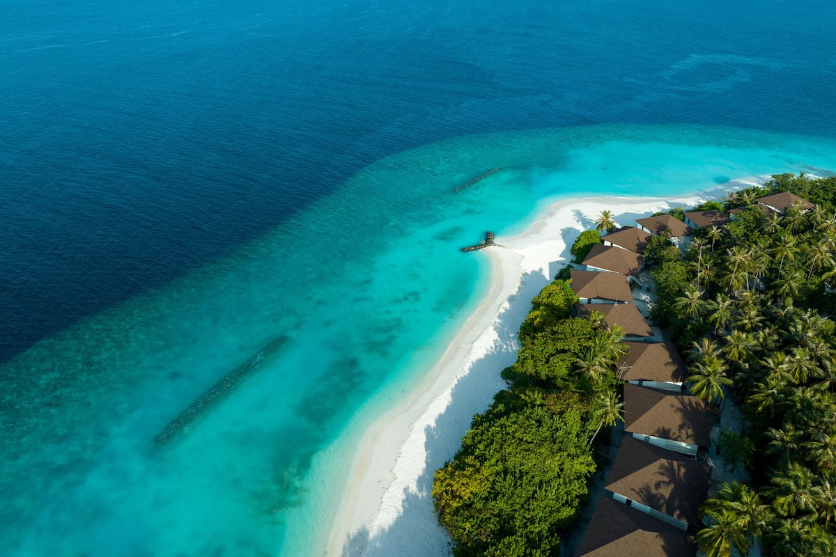 An aerial view of a coastal resort with a white sandy beach, clear turquoise waters, and lush greenery.