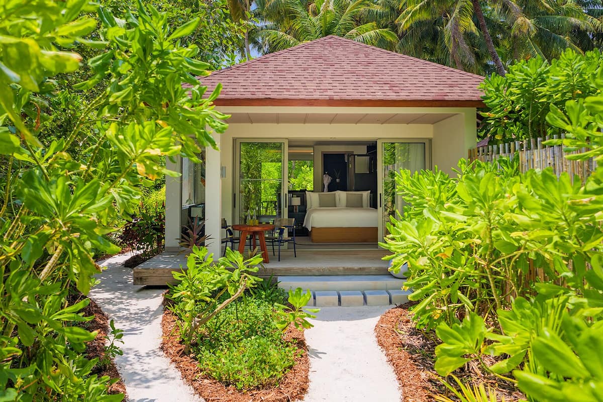 A small, single-story structure with a tiled roof, a bed, and a table with chairs in the center.