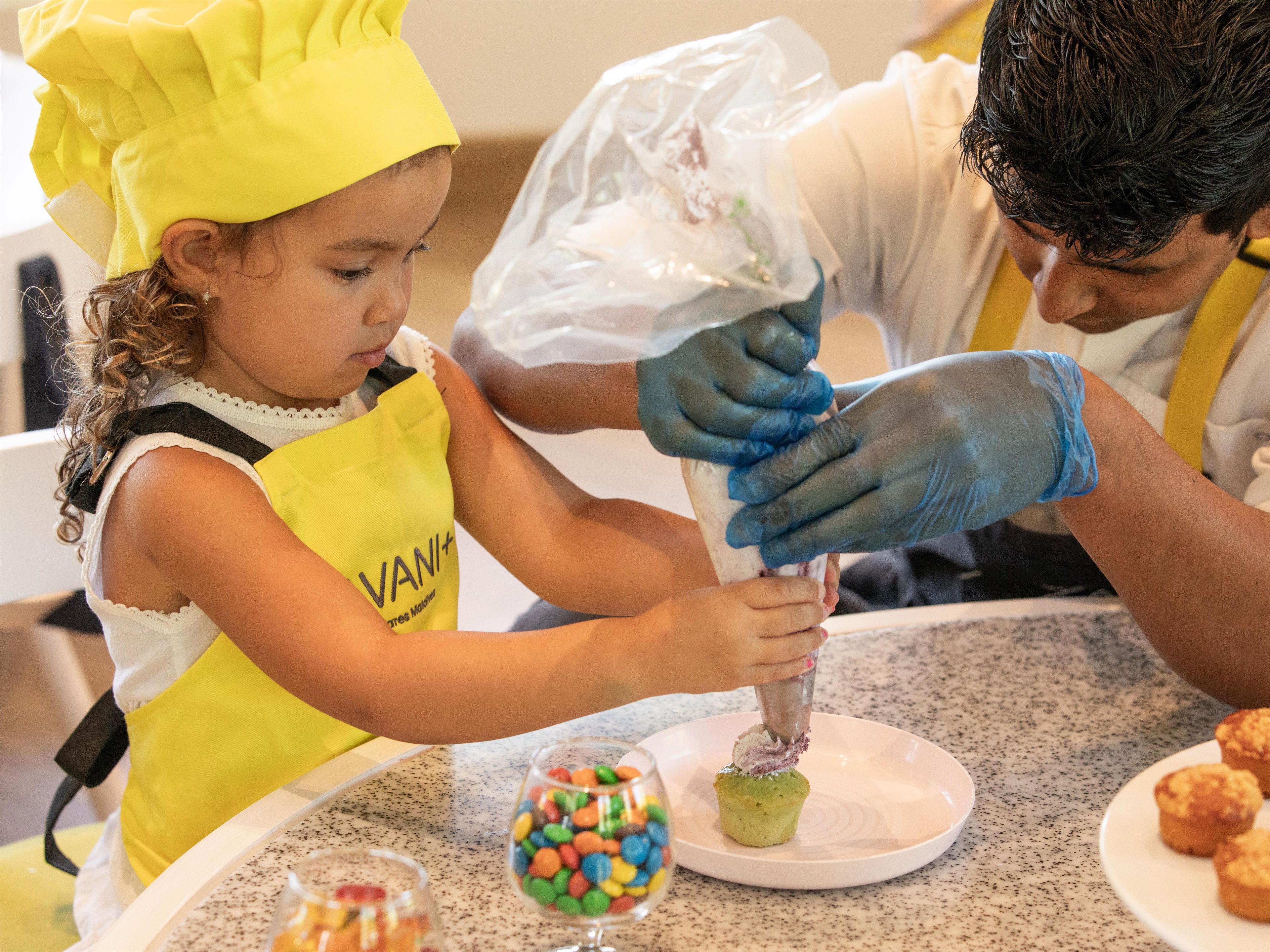 A person in a yellow chef's hat and apron preparing food with a plastic bag.