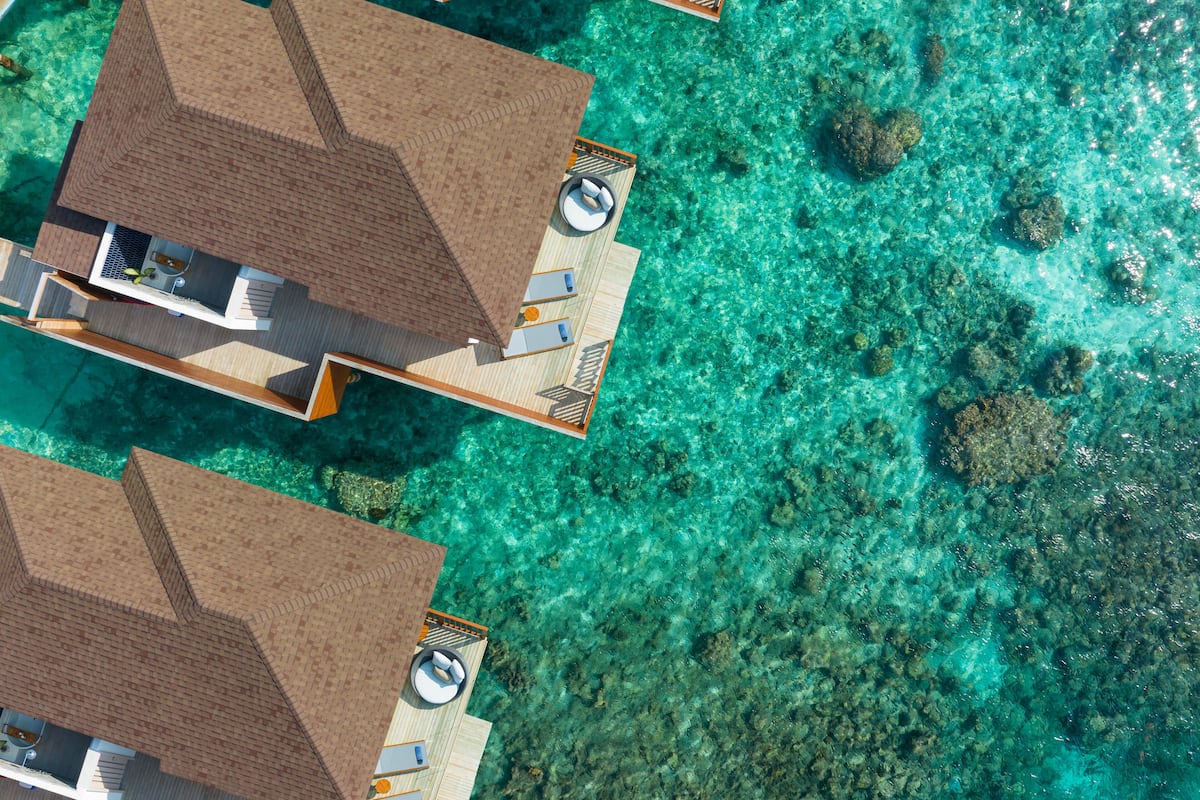 An aerial view of overwater bungalows with clear turquoise water, wooden deck flooring, and a small pool area.