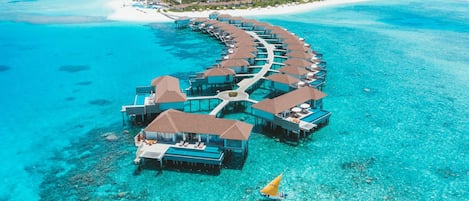 Ein Überwasser-Resort mit mehreren Bungalows, die durch Gehwege verbunden sind, inmitten von klarem türkisblauem Wasser.