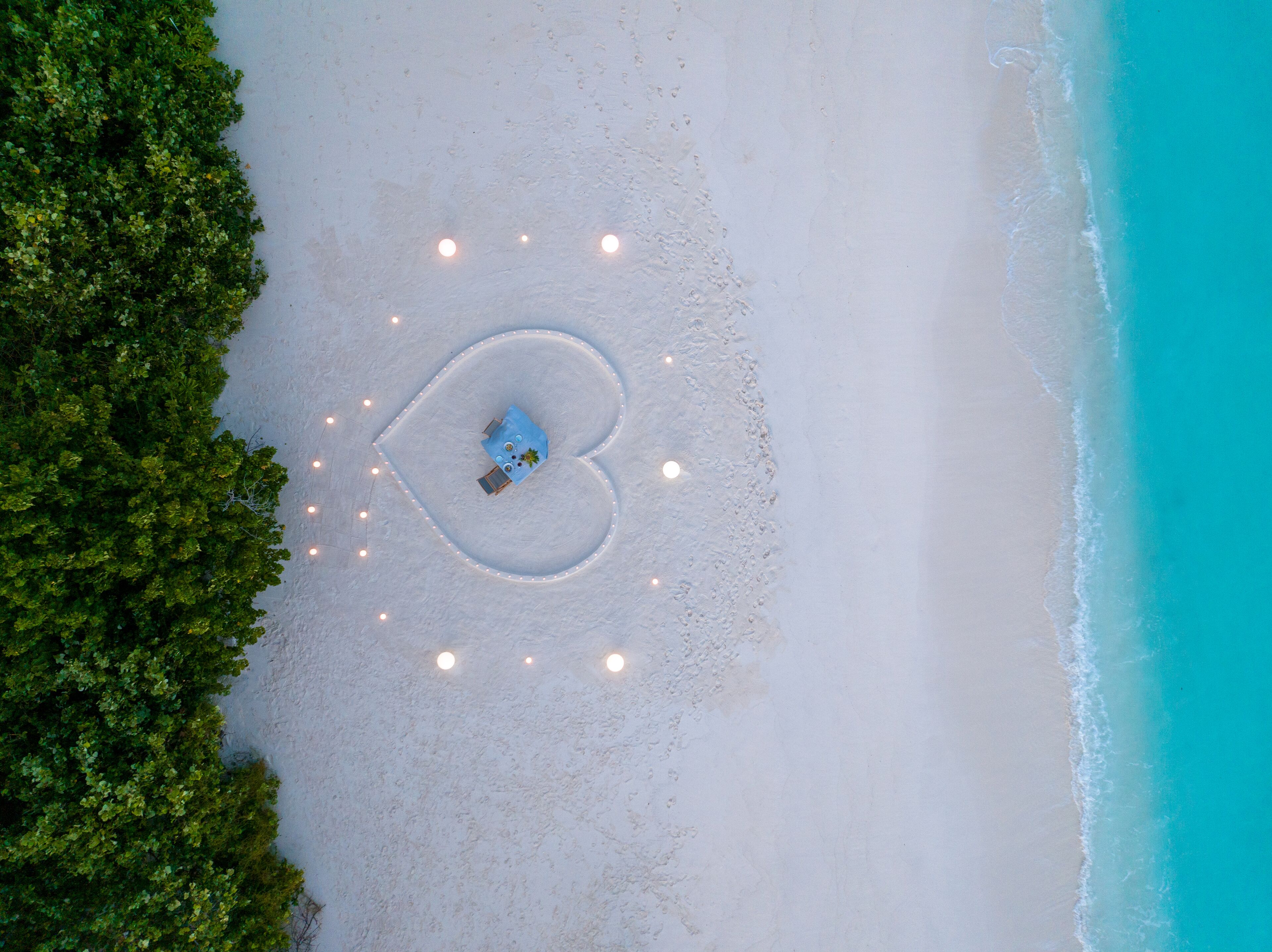 An aerial view of a beach with a heart-shaped light arrangement and a small structure.