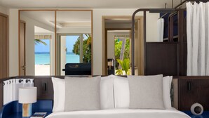 A hotel room with a bed, a nightstand, a lamp, a clock, and a view of the beach. - Avani+ Fares Maldives Resort (Fares)