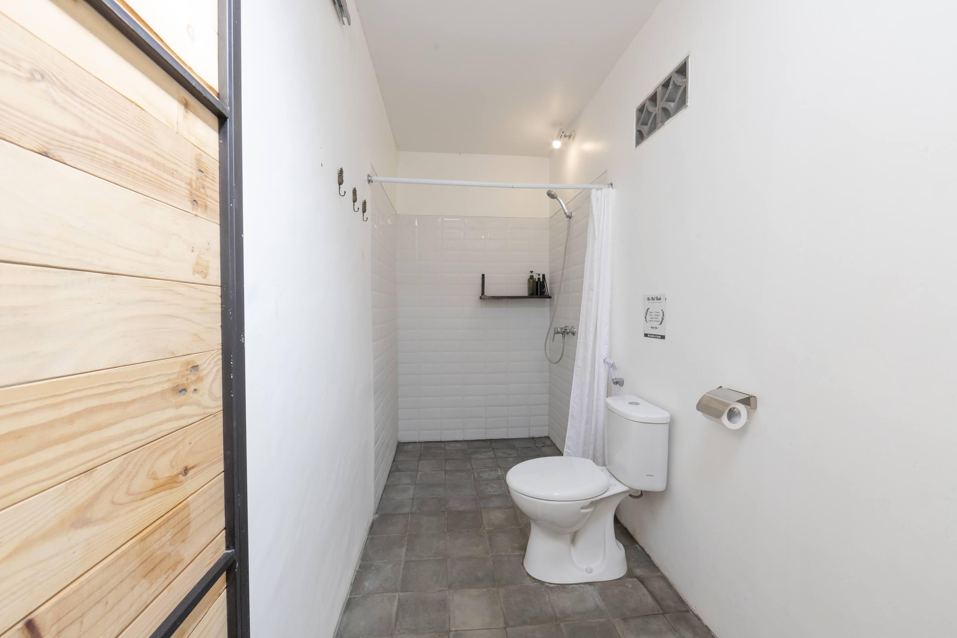 A compact bathroom with a white toilet, a shower area, and a wooden wall.