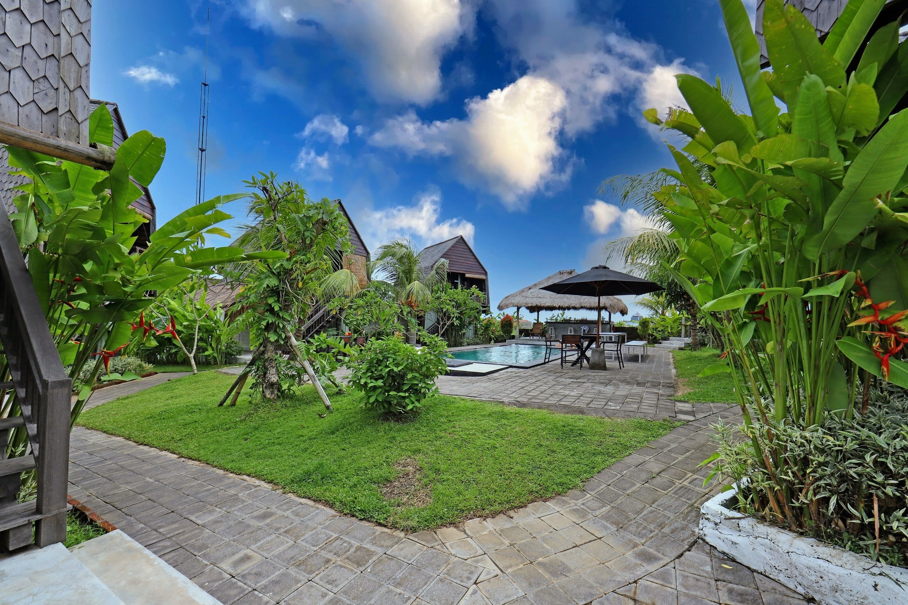 A well-maintained garden with a swimming pool, a barbecue area, and a thatched-roof structure.