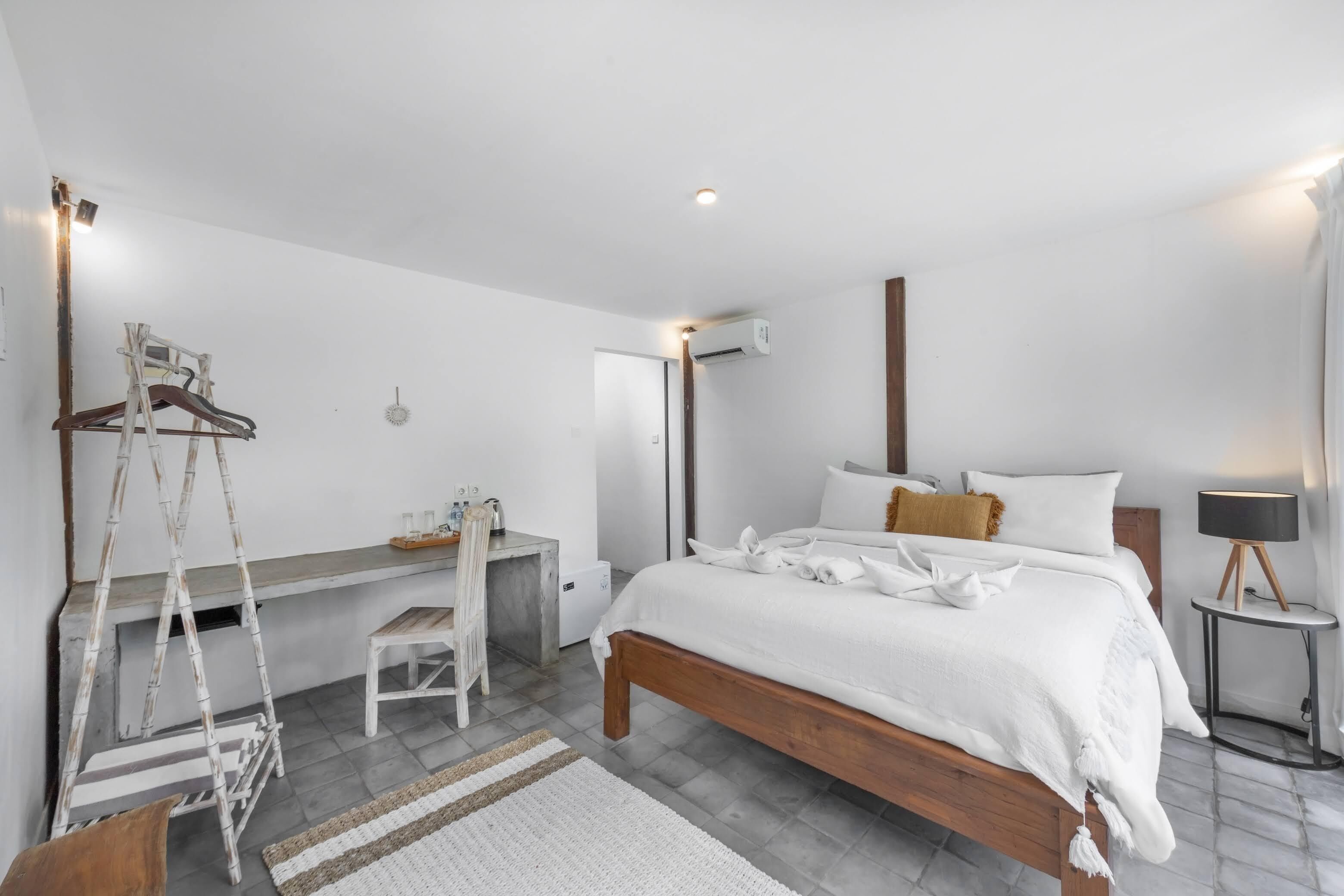 Een moderne slaapkamer met een houten bed, wit beddengoed, een bureau met stoel, en een airconditioner.