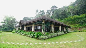A traditional house with a tiled roof, surrounded by a well-maintained garden with various plants and a stone pathway. - Magnolia Estates & Resort (Virajpet)