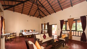 A spacious room with a high ceiling, a bed, a sofa, a coffee table, and a dining area. - Magnolia Estates & Resort (Virajpet)
