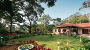 A garden with a pond, a covered seating area, and a building with a red roof. - Magnolia Estates & Resort (Virajpet)