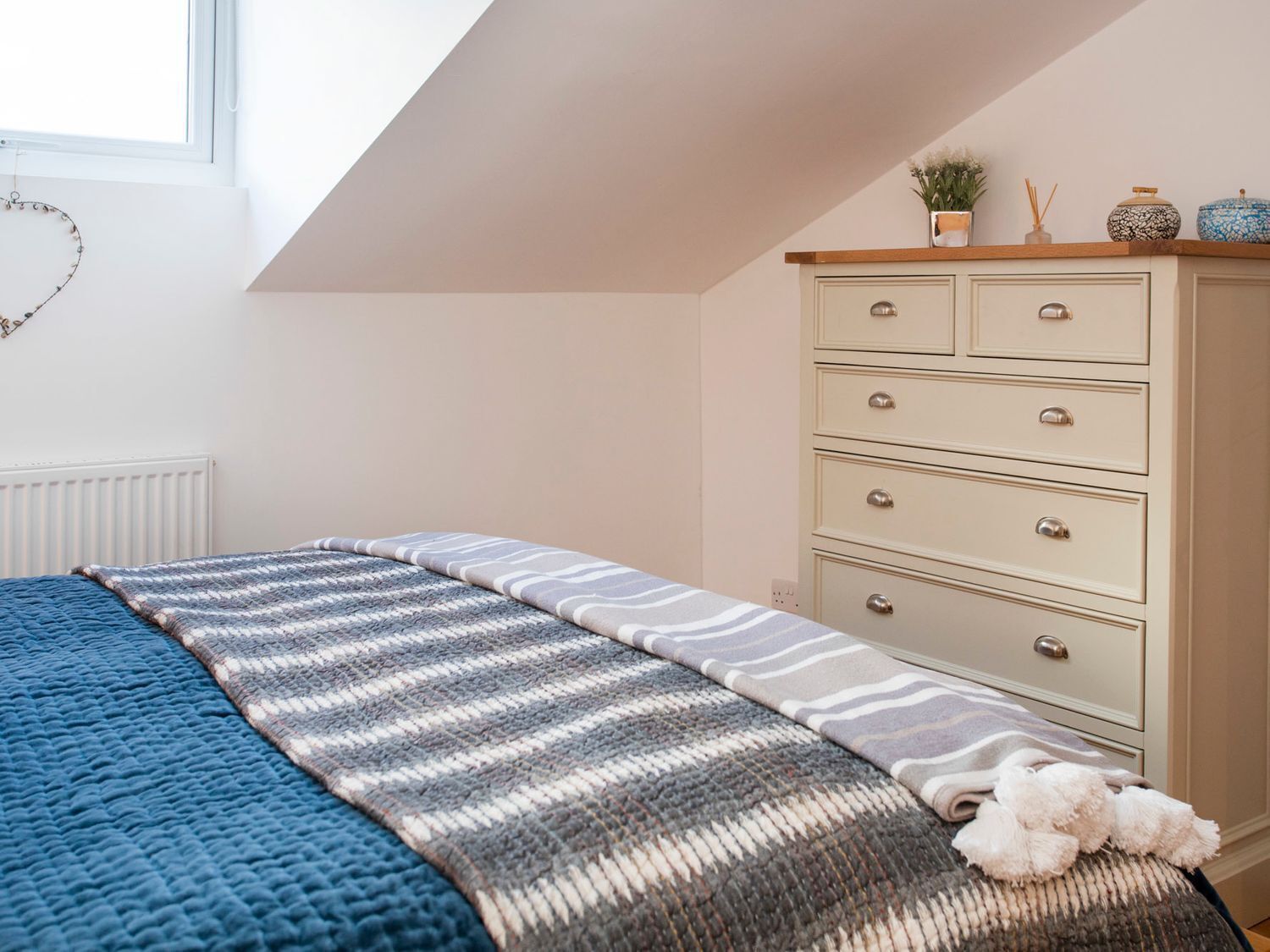 Een slaapkamer met een bed, een dressoir en een raam.