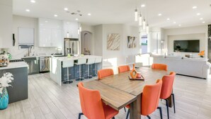 Una cocina moderna con armarios blancos, una isla central y una zona de comedor con sillas naranjas.