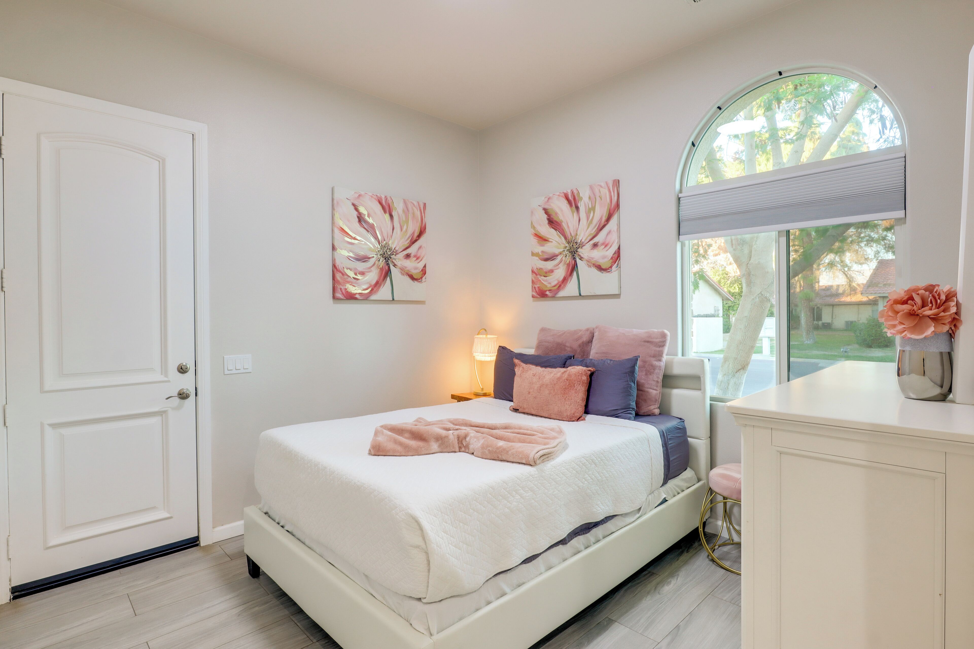 A bedroom with a bed, a nightstand, a dresser, and a window with a view of trees.