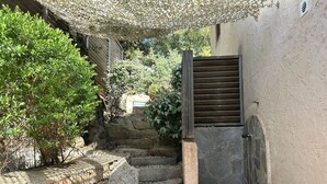 Ein schmaler Steinweg führt zu einem hölzernen Tor, umgeben von viel Grün und einer rustikalen Steinmauer.