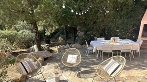 Eine Terrasse im Freien mit Steinboden, Korbstühlen, einem Esstisch und Lichterketten.