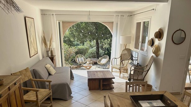 Ein gemütliches Wohnzimmer mit einer Couch, Sesseln, einem Holztisch und Blick auf einen Garten durch einen Bogen.