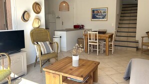 Ein gemütliches Wohnzimmer mit Fernseher, Korbmöbeln, einem Essbereich mit Tisch und Stühlen, einer Küche mit Kühlschrank und einer Treppe.