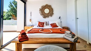 Un dormitorio moderno con una cama grande, una mesita de noche de madera, un espejo redondo y vistas al exterior.