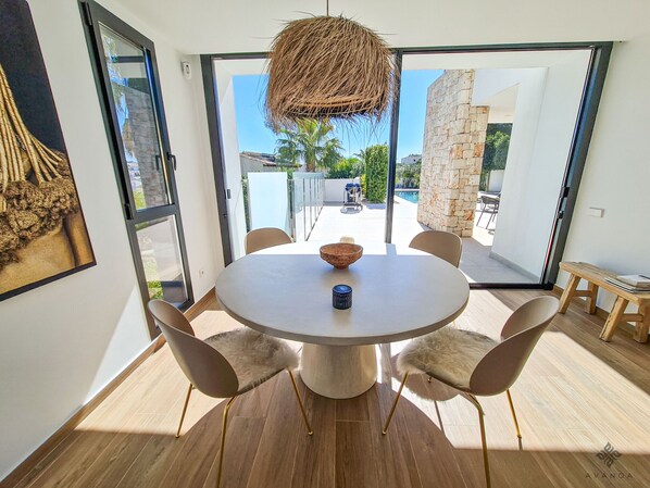 A modern dining area with a round table, six chairs, a hanging light fixture, and a view of the outdoor patio.