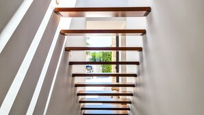 Un interior moderno con una escalera que baja a un nivel inferior, con vigas de madera y tragaluces.